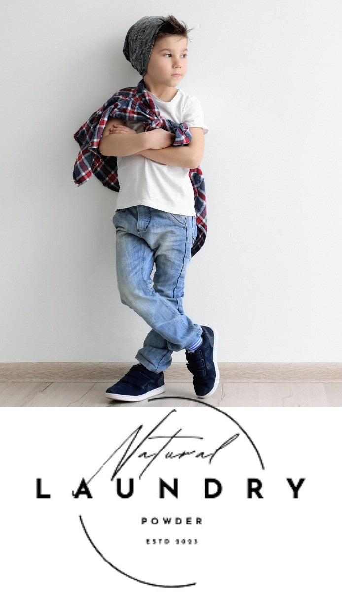 A child stands against a white wall wearing a gray beanie, white T-shirt, blue jeans, and dark sneakers, with a red plaid shirt draped over the shoulders. Below the photo is a large logo reading 'Natural LAUNDRY POWDER ESTD 2001'.